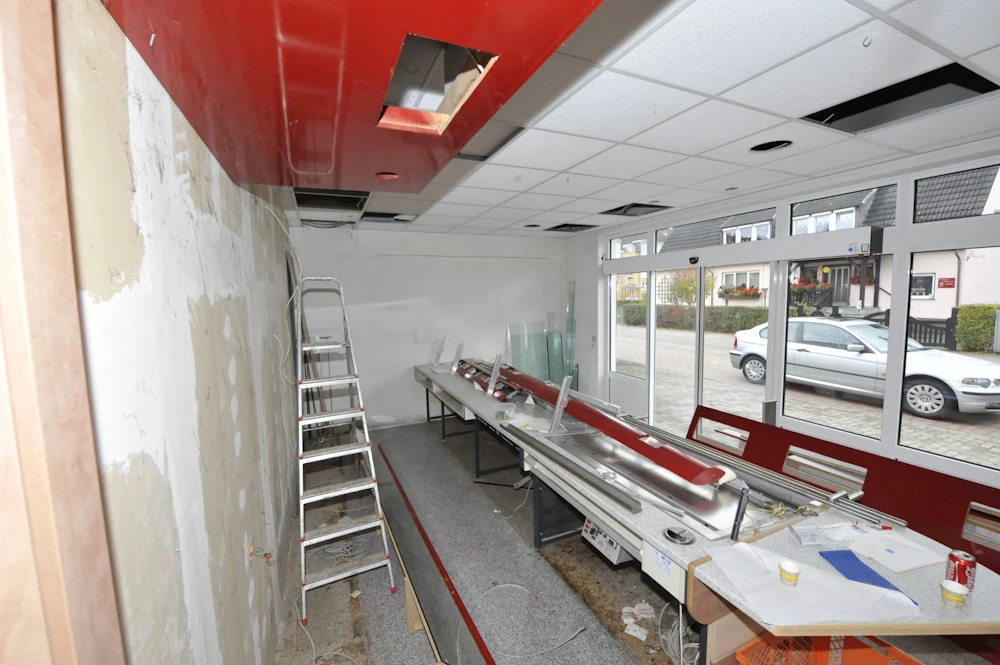 umbau-baeckerei-arztpraxis-05 Ehemaliger Verkaufsraum während des Rückbaus mit Thekenresten, Leiter und Schaufensterfront