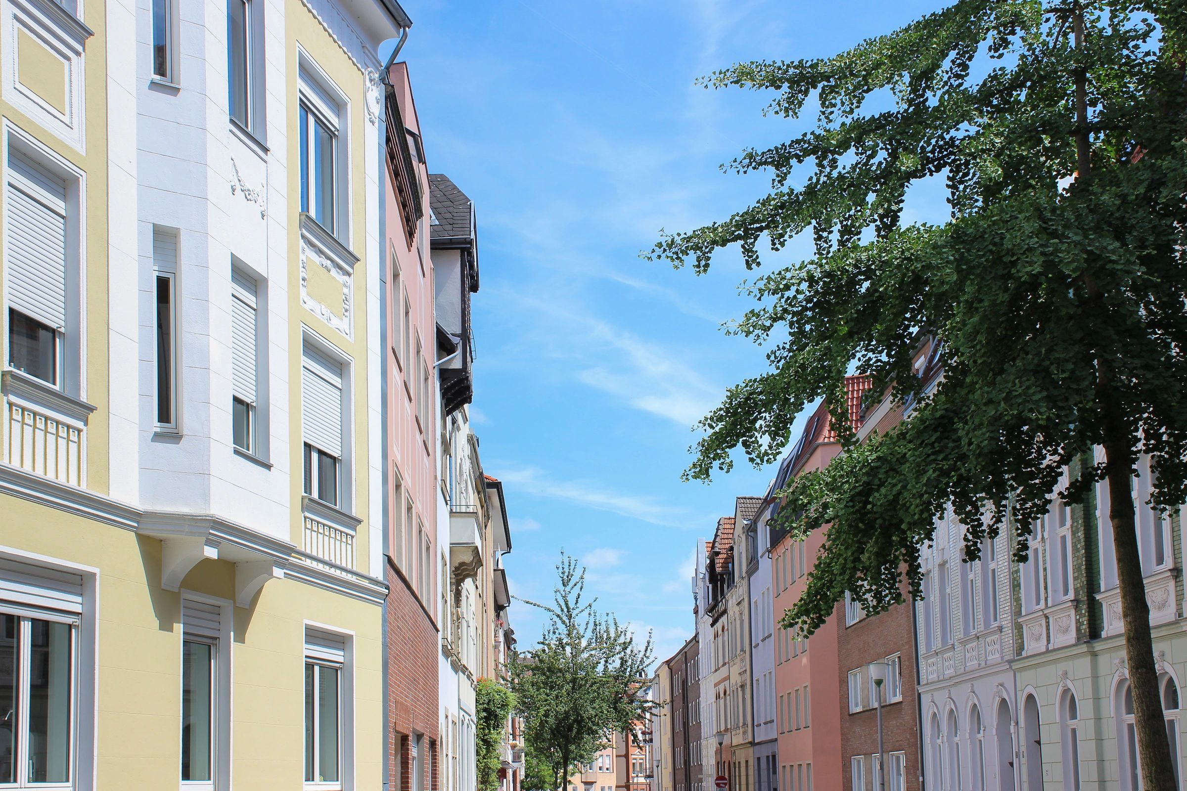 Farbenfrohe Altbauhäuser in einer baumgesäumten Straße in Münster.
