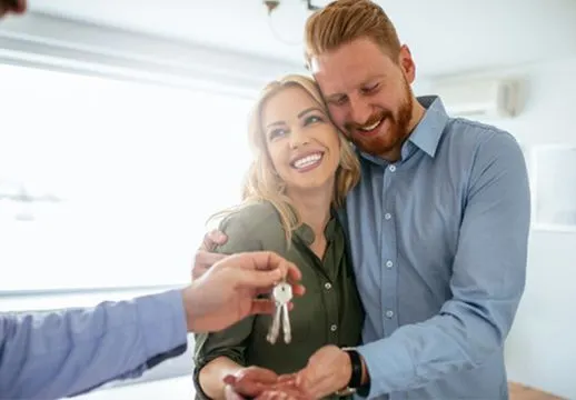 Ein glückliches, junges  Paar nimmt den Schlüssel zu einer Mietwohnung entgegen.