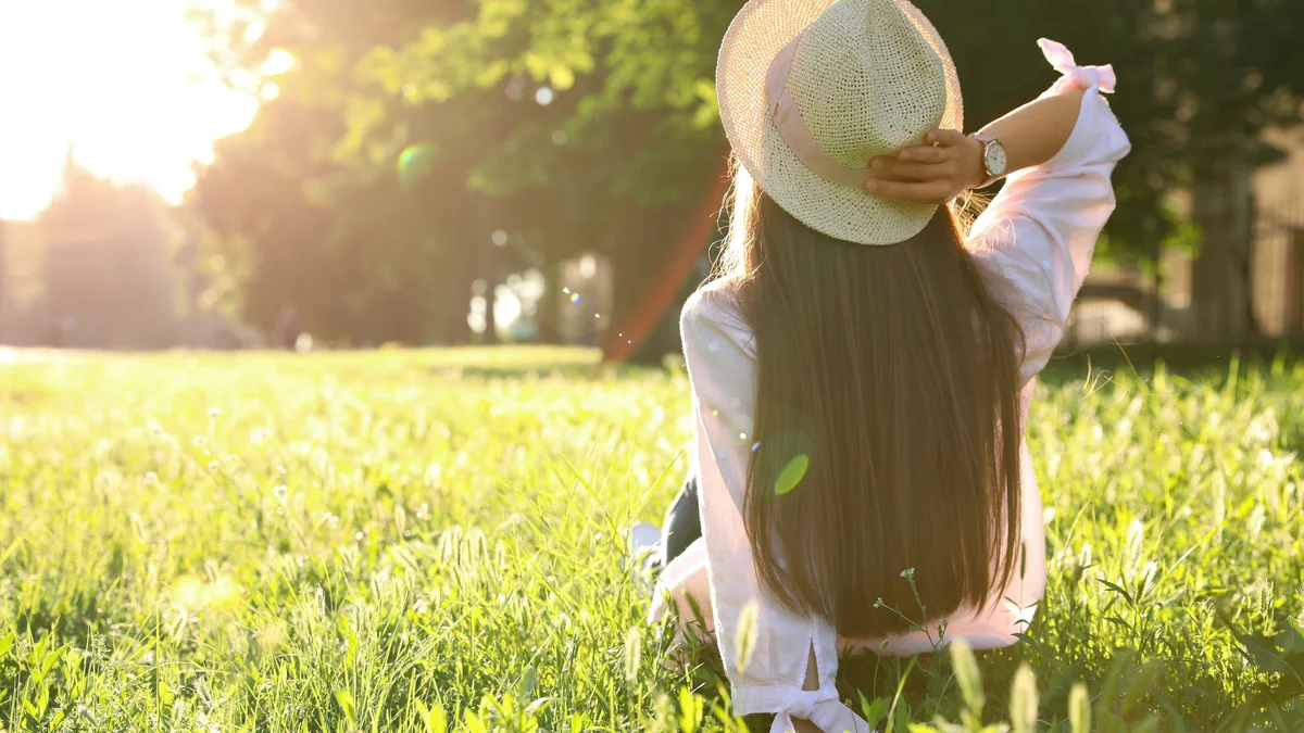 Frau mit Sonnenhut sitzt im sonnigen Garten