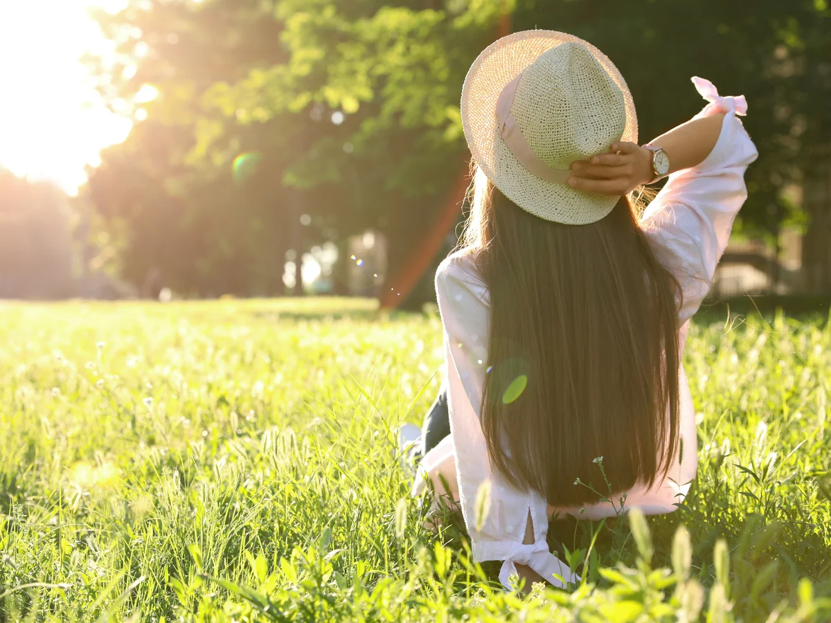 Frau mit Sonnenhut sitzt im sonnigen Garten
