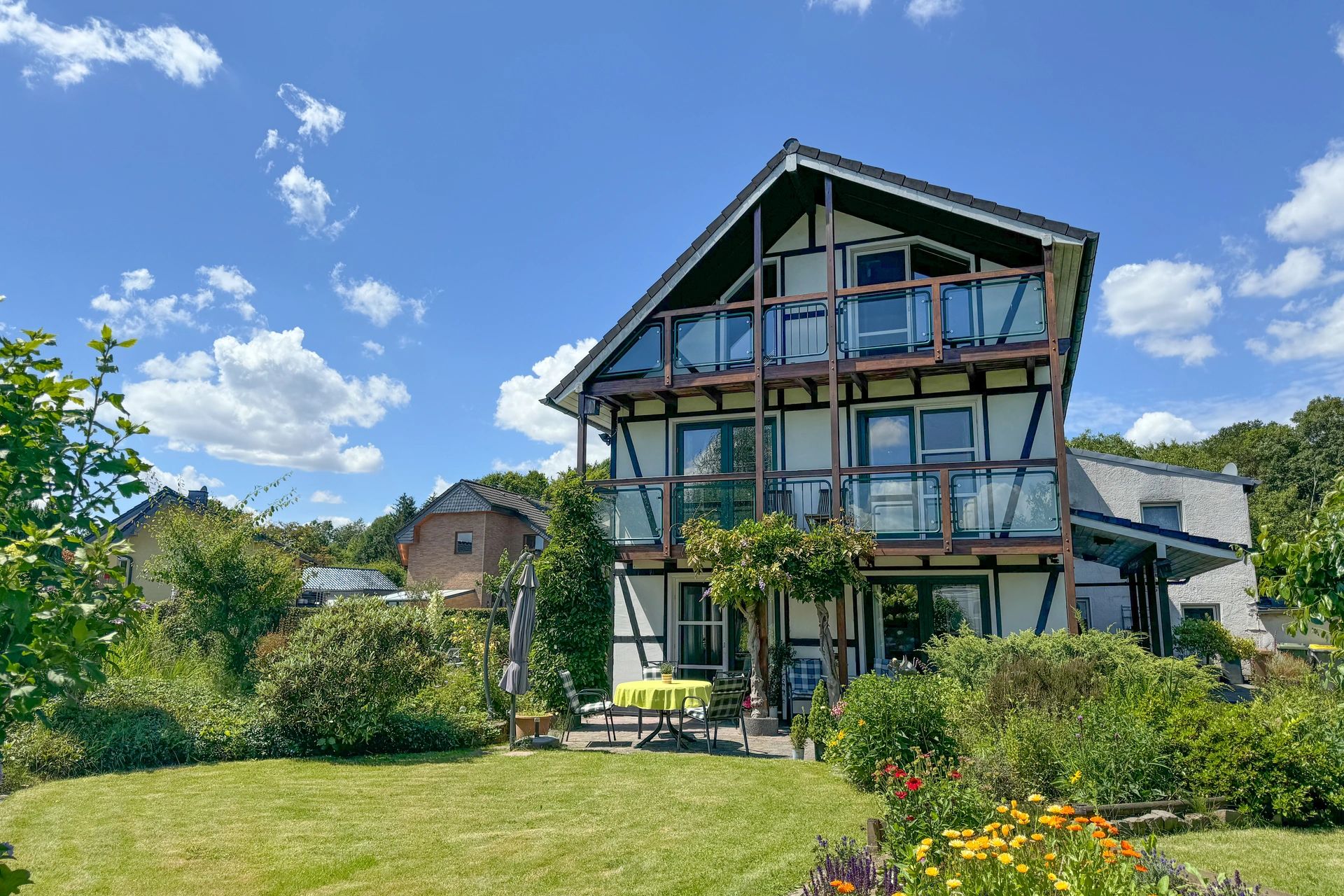 Dreistöckiges modernisiertes Fachwerkhaus mit Glasbalkonen, umgeben von gepflegtem Garten und Blumen.