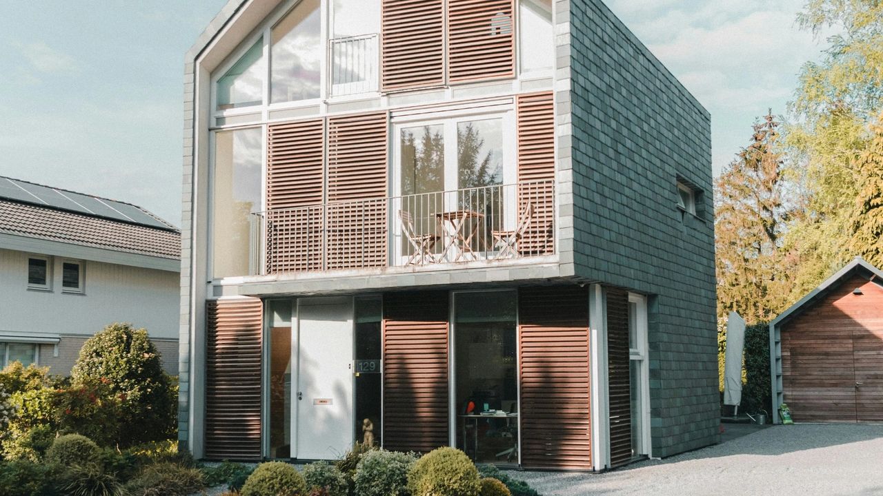 ernes Einfamilienhaus mit großer Glasfront, Holzverkleidung und gepflegtem Vorgarten bei Tageslicht