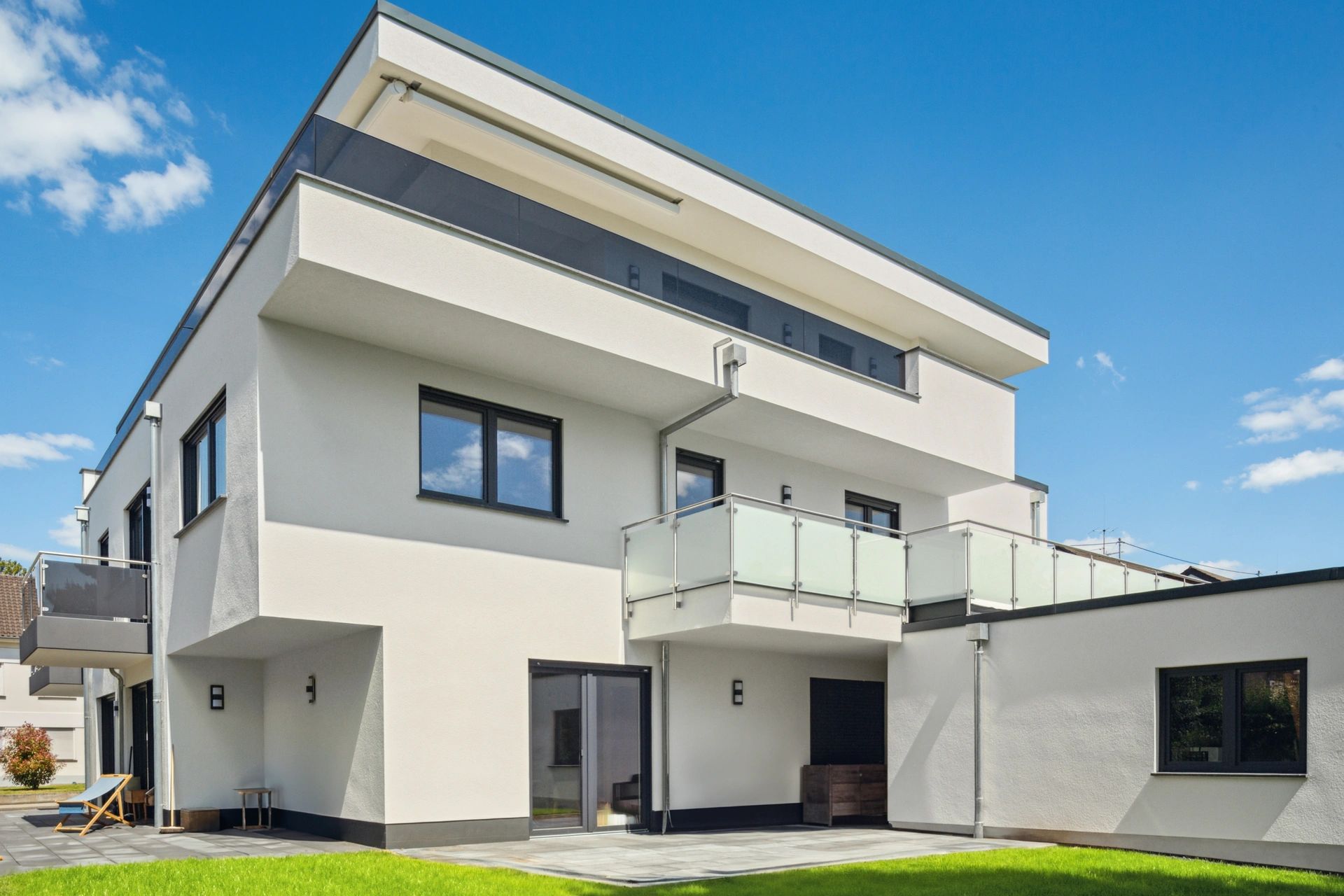 Neubau mit klaren Linien, Glasbalkonen und Rasenfläche im Gartenbereich.