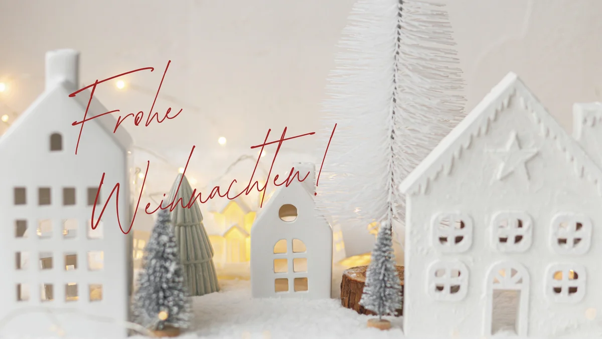 Weiße Deko-Häuser im Schnee mit dem Schriftzug Frohe Weihnachten