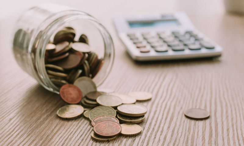 liegendes Glas mit Cent-Stücken und einem danebenliegenden Taschenrechner