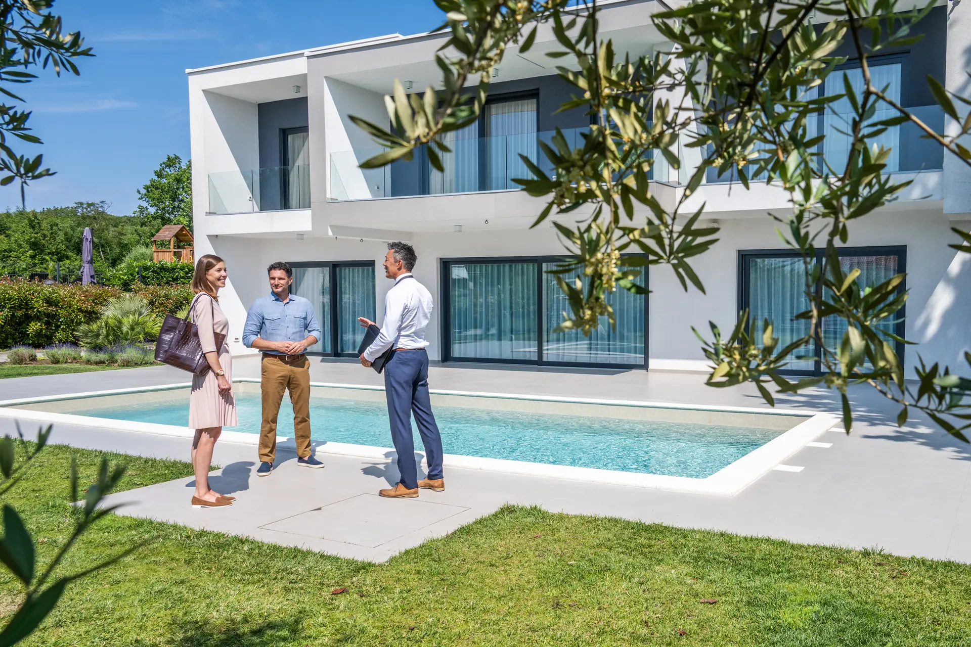 Male real estate agent talking with couple Paar mit einem Immobilienmakler im Garten einer Villa mit Pool