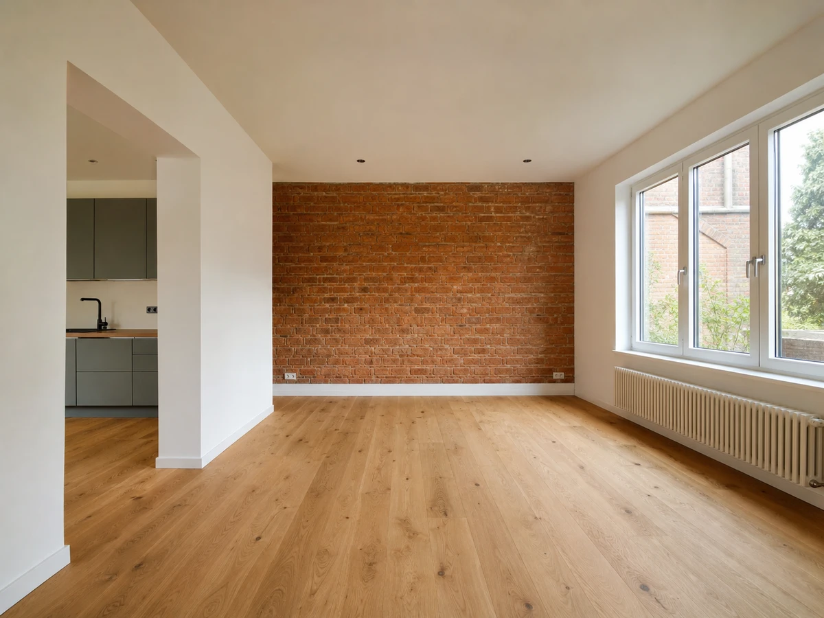 wohnwerte-niederrhein-sanierter-wohnraum Sanierter Wohnbereich mit Backstein-Akzentwand, neuen Eichendielen und moderner Küche im Hintergrund