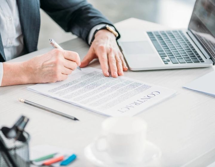 Unterzeichnung eines Vertrags mit ausgeklapptem Laptop auf einem Schreibtisch