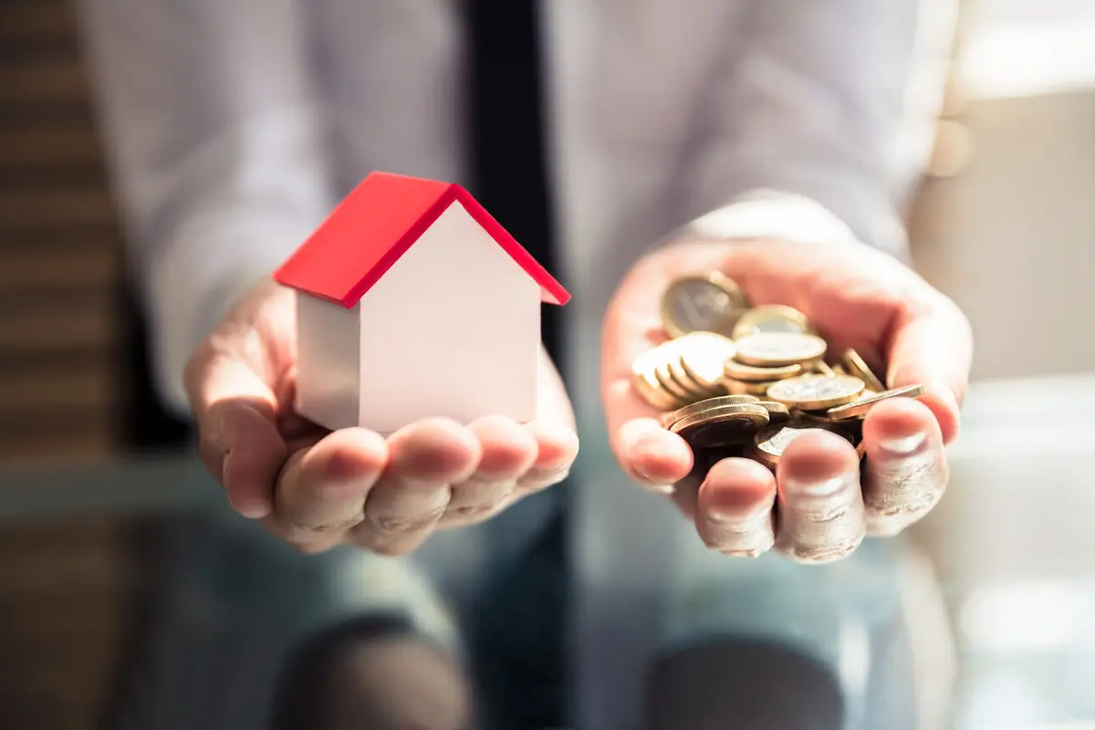 Businessperson Holding House Model And Golden Coins Eigentumswohnung verkaufen