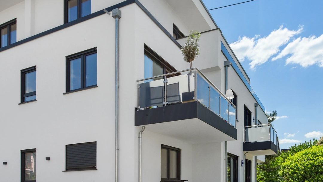 Weißes Mehrfamilienhaus mit moderner Architektur, großem Balkon und gepflasterter Einfahrt.