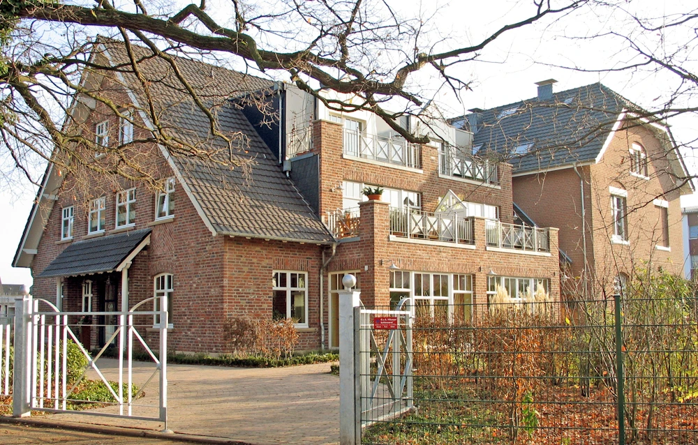 mehrfamilienhaus-17 Klinker-Mehrfamilienhaus mit Giebeln und Balkonen hinter Tor und Bäumen
