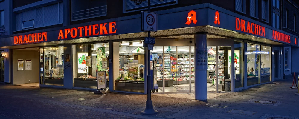 geschaeftshaus-21 Eckladen einer Apotheke am Abend mit beleuchteter Schrift „Drachen Apotheke“