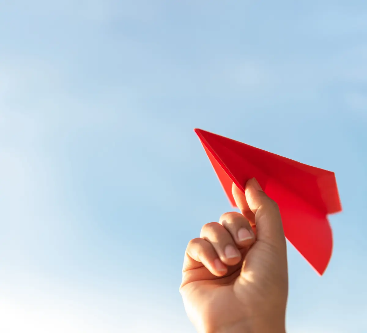 Woman Hand holding red paper rocket with blue sky background. freedom concept. Flieger in der Hand