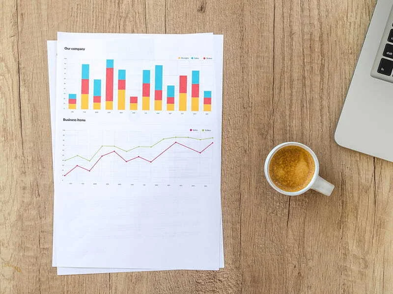 Ausgedruckte Statistiken neben Laptop und Kaffeetasse