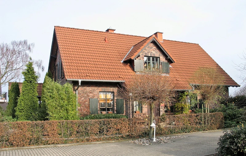 einfamilienhaus-22 Klinkerhaus mit rotem Ziegeldach, Zwerchgiebel und Holzläden hinter Hecke