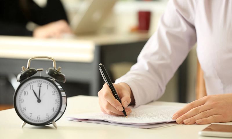 Notizen machende Person / Ein Wecker im Vordergrund