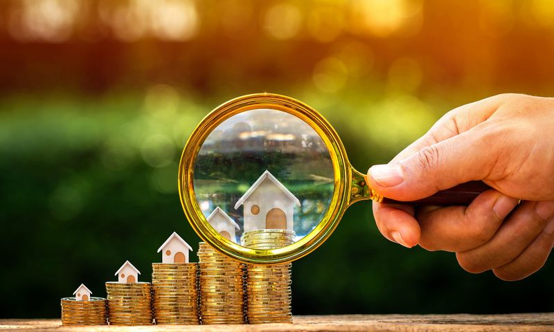 Lupe vor einem kleinen Modell-Holzhaus, was auf einem Münzturm steht.