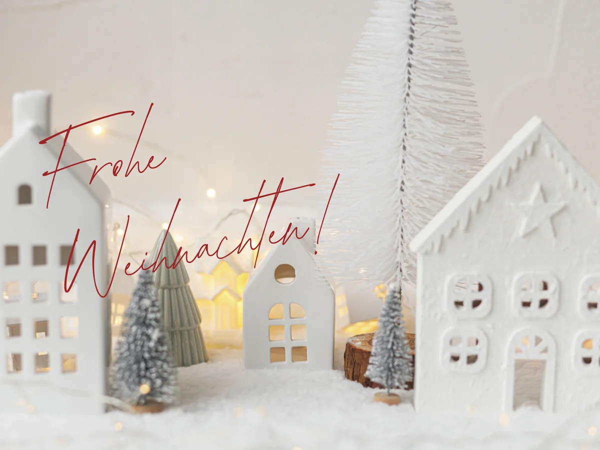 Weiße Deko-Häuser im Schnee mit dem Schriftzug Frohe Weihnachten