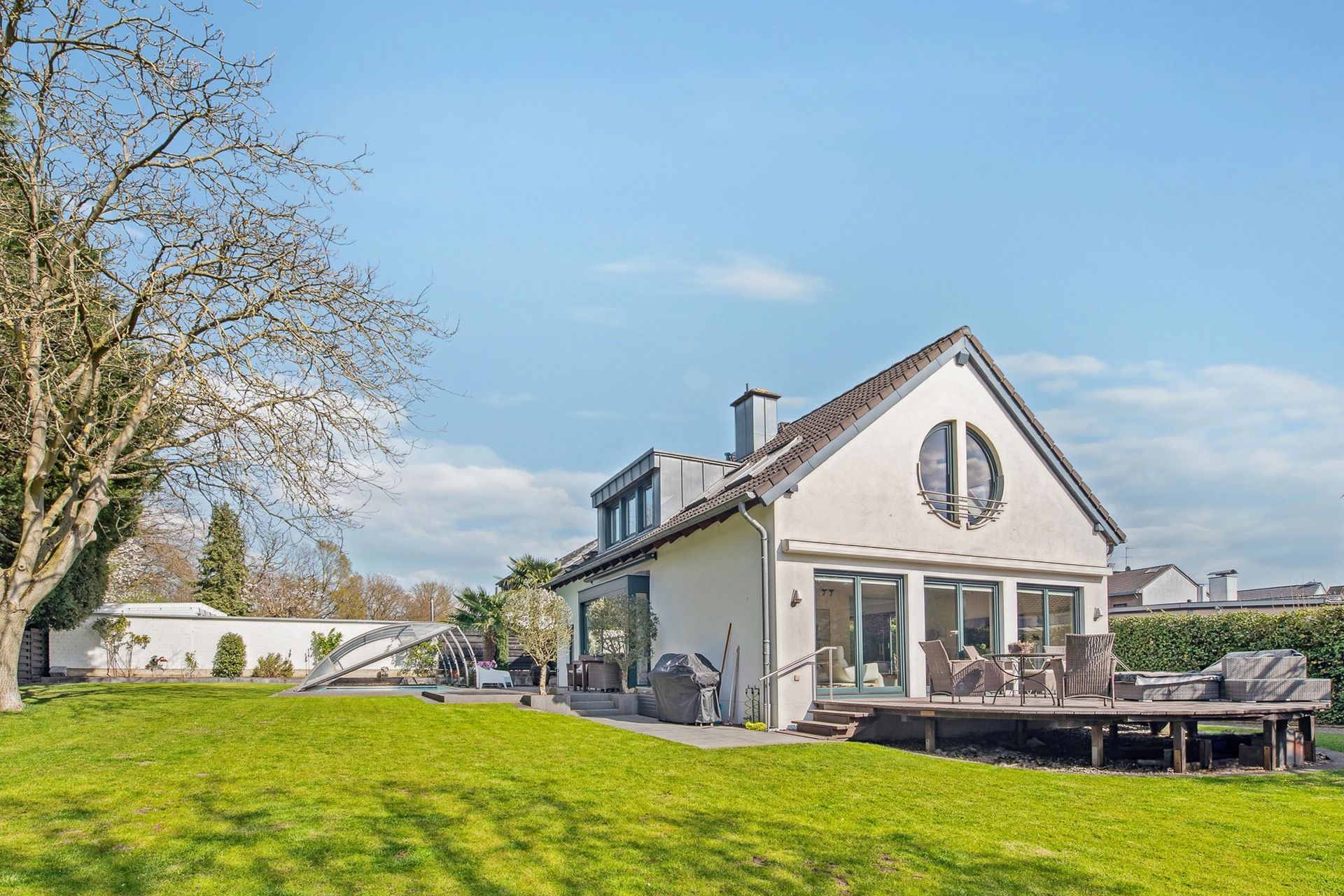 Großes Einfamilienhaus mit rundem Giebelfenster, moderner Terrasse und weitläufigem Garten.